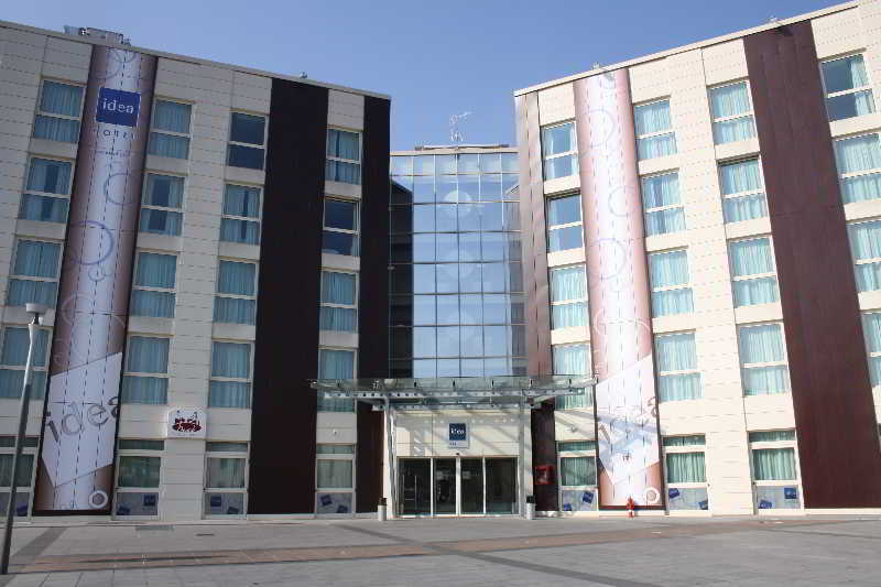 Idea Hotel Milano Malpensa Airport Case Nuove  Eksteriør billede The photo shows a modern hotel building with a prominent glass entrance. The façade features a mix of materials, including light-colored stone and dark panels. Large banners or displays adorn the sides of the building, adding visual interest. The are